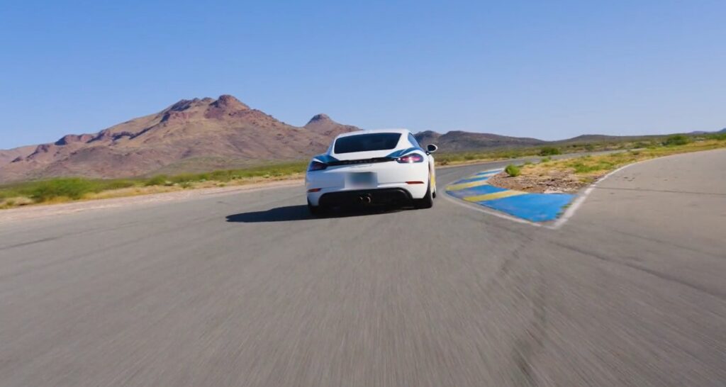 A Porsche Cayman exiting a corner at INDE Motorsports Ranch with the mountains behind